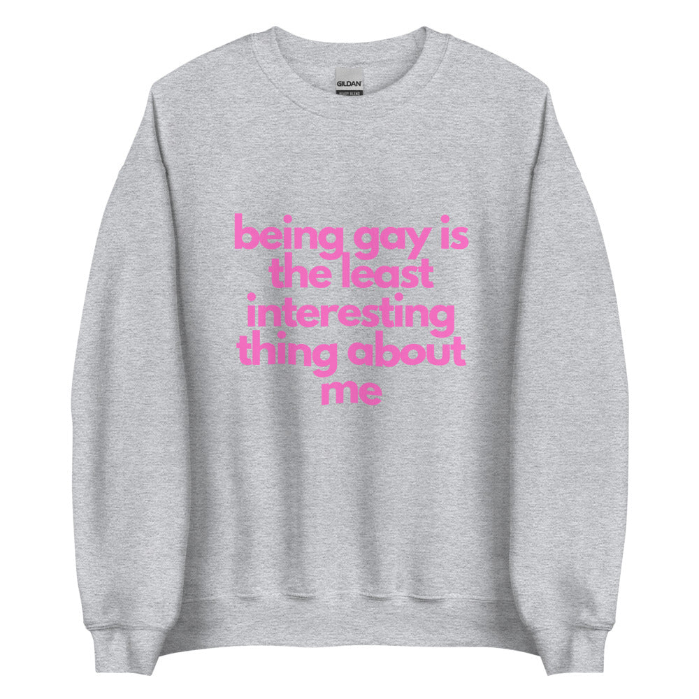 This is a pride apparel crewneck sweatshirt. It is grey and has "being gay is the least interesting thing about me" written across the front in pink letters.